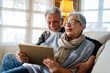 © NDABCREATIVITY - Elderly couple enjoying a tablet. Senior man and woman smiling, bonding over technology.