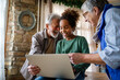 © NDABCREATIVITY - Happy senior couple using modern tech gadget laptop together with grandchild at home.