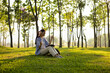© Kield KD - A woman is sitting on the grass in a park, listening to music. She is wearing headphones and has a book in her lap. Concept of relaxation and leisure