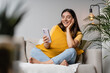 © Andrei - Digital self-care at home. Latina Indian woman in her 20s on sofa with phone, tuning into online therapy or study, blending mental wellness and digital learning in a chill home setup