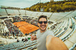 © Davide Angelini - Handsome young tennis spectator taking selfie picture watching grand slam tournament match at the stadium - Sport and technology life style concept