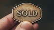 © Tanakrit - A close-up of a hand holding a bronze sign or badge with the word 'SOLD' engraved on it.