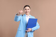 © New Africa - Real estate agent holding key with house shaped keychain and folder on beige background