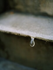 Fototapete - A single, transparent drop of water hangs precariously from a weathered, grey stone surface, reflecting a blurred background. : Generative AI