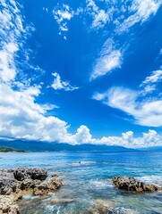 Fototapete - Stunning coastal scene featuring turquoise ocean water lapping against rocky shoreline under a vibrant blue sky with fluffy white clouds and distant mountains. : Generative AI