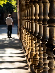 Aufkleber - Sunlight illuminates a row of ornate stone balusters, a blurred figure walks in the background, creating a captivating interplay of light and shadow. : Generative AI
