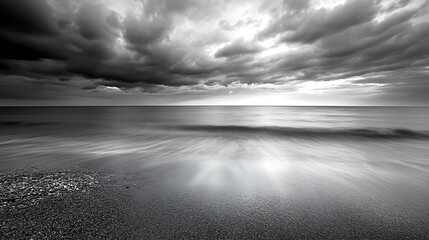 Leinwandbilder - Dramatic grayscale seascape: dark clouds over a tranquil ocean meeting a pebble beach at sunset, showcasing the serene beauty of nature's contrast. : Generative AI