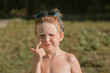 © Mariia Andreeva - Close-up of little white-skinned boy in sunglasses applying sunscreen to his face and nose on a sunny day. Concept of child sun safety, skincare, and summer protection.