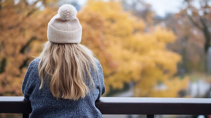 Poster - Woman with blonde hair wearing a beige knit beanie with pompom, stands at a railing overlooking autumnal trees. : Generative AI
