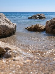 Poster - Tranquil coastal scene featuring sunlit rocks partially submerged in clear, shallow water, with a calm blue sea in the background on a bright sunny day. : Generative AI