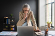 © InsideCreativeHouse - Thoughtful mature business woman entrepreneur in office using laptop at work, professional middle aged 50 years old female company executive wearing suit working on computer at workplace.
