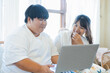 © Sumala - Asian couple using laptop together at home enjoying lifestyle activity with happy lgbtq connection and warm natural light