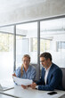 © Stock 4 You - Team of mature businessman and accountant woman discussing financial tax document report sitting at table in office. Two colleagues professional business people working together on project. Vertical