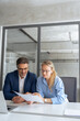 © Stock 4 You - Two professional business people working together. Partners mature man and woman discussing financial document report sitting at table in office. Team leader explain trainee working process. Vertical