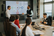 © qunica.com - A diverse group of business people in a modern office setting engaged in a strategic meeting, focusing on collaborative discussion and presentation insights.