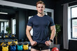 © Alex & M Studio - Confident athletic man with blonde hair standing in a modern well-equipped gym fitness center, looking directly at the camera, representing strength and healthy workout focus