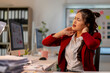 © Wasana - A woman in a red jacket is sitting at a desk with her head in her hands