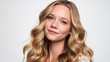 © liliyabatyrova - A blonde woman with long wavy hair smiles softly while posing in a well-lit studio. The background is neutral, accentuating her features and creating a warm atmosphere