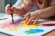 © Yuliia - A vibrant masterpiece in the making: A close-up of a young child's hands holding colorful paintbrushes and creating art on canvas.