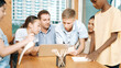 © InfiniteFlow - Caucasian teacher giving advise to young student while boy lecture comment. Professional instructor write comment surrounded by multicultural children at table with laptop and paper. Edification.