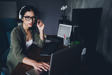 young female professional working at a computer in a home office environment with headphones and cas