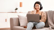© Prostock-studio - Technology Concept. Smiling asian woman listening to music, using laptop, sitting on couch in living room. Millennial woman enjoying her favorite song or having video conference call online at home