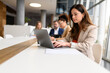 © Moon Safari - Focused female lawyer working online on laptop in boardroom while colleagues collaborate in the background