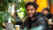 © lek Rinto - Smiling young man working on laptop in a cafe, surrounded by plants