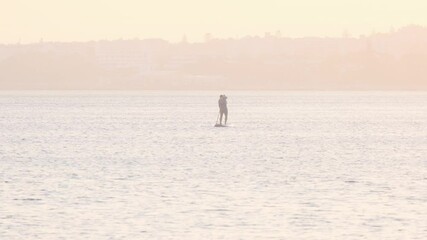 Wall Mural - golden hour light bathing lone paddle boarder gliding across tranquil portuguese waters, capturing s