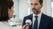 © Annada - Man in suit speaks into microphone held by woman in office setting.
