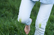 © HalynaRom - A person stands in lush green grass, showing grass stains on their white jeans. The bright sunlight highlights the vibrant colors of the outdoor setting, suggesting playful activities.