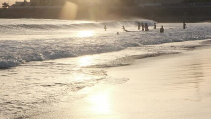 Wall Mural - golden sunlight reflecting on wet sand, capturing relaxed tourists playing in gentle waves during pi