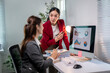 © Wasana - Two women are sitting at a desk with a computer monitor in front of them