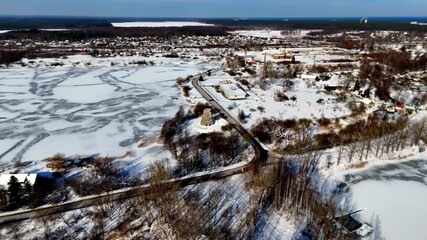 Wall Mural - A frozen lake with winding ice patterns and a nearby small town surrounded by snow-covered fields under clear winter skies, captured from an elevated aerial view.