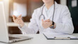 © bongkarn - Close up of a doctor with stethoscope explaining with hand gesture while sitting at the white table in diagnosis room