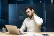 © Tetiana - A tired young man sits in the office at his desk, rubbing his neck with his hand, feeling a dull pain and tension