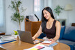 © Apichat - A woman is sitting at a desk with a laptop and a stack of papers