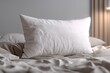 © whitestorm - A pristine white pillow resting on a rumpled bed with textured linens in a muted color palette creating a serene and inviting atmosphere in a calming bedroom scene.