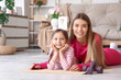 © Pixel-Shot - Sporty young mother and her cute little daughter lying on yoga mat at home. Mother Day celebration