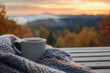 © Premium AI - Warm coffee mug resting on a cozy blanket with a serene autumn sunset in the background