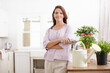 © peopleimages.com - Pot, plants and woman in portrait by kitchen counter, maintenance and pruning for gardening in home. Mature person, watering can and flowers for growth, sustainability and arms crossed in house