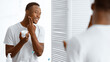 © Prostock-studio - African American Man Using Facial Cream Moisturizer Caring For Face Skin Standing Near Mirror In Modern Bathroom Indoors. Male Skincare And Men's Daily Beauty Routine Concept. Panorama