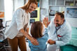 © Davor - Smiling doctor using stethoscope to check young girl at medical clinic with mother nearby