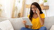 © Prostock-studio - Pretty black lady using tablet computer for online work, education or entertainment while talking on smartphone at home. African American woman with modern gadgets indoors