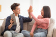 © Prostock-studio - Asian Couple With Digital Tablet Giving High Five Celebrating Success Sitting On Couch In Living Room At Home. Good News Celebration And Joy Of Victory Concept.