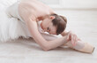 © Prostock-studio - Beautiful graceful young ballerina in pointe shoes at white wooden floor makes ballet leg stretching. Ballet practice of classical dancer.