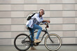 © Prostock-studio - Cheerful black guy with backpack and headphones riding bicycle near brick wall on city street