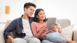 © Prostock-studio - Cheerful Korean Couple Using Digital Tablet Computer Watching Movie Relaxing On Day-Off Sitting On Sofa At Home. Asian Family Browsing Internet Together In Living Room On Weekend