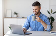 © Prostock-studio - Handsome smiling businessman drinking coffee and using laptop in office, checking emails on computer, sitting at desk, free space