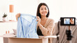 © Prostock-studio - Fashion And Style Blog. Asian young woman vlogger recording unpacking video on camera device at home, female model influencer shooting brand advertising promo. Lady showing clothing after unboxing